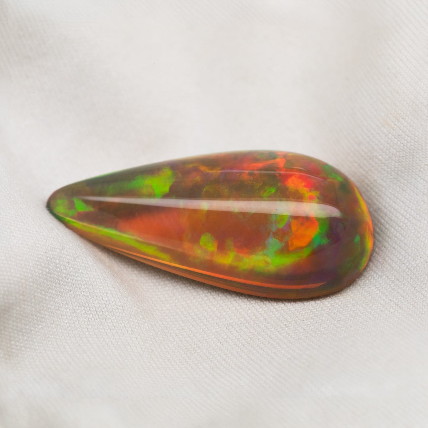 Pear-shaped multicolor opal cabochon on a white fabric background