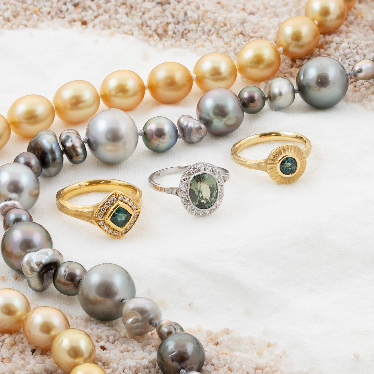 Pearl necklaces and rings on a sandy surface