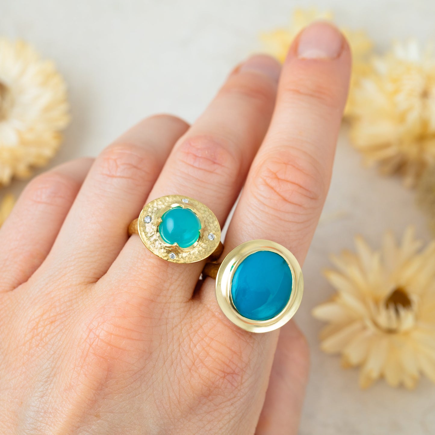 Gold rings with blue stones on a hand, with dried flowers in the background