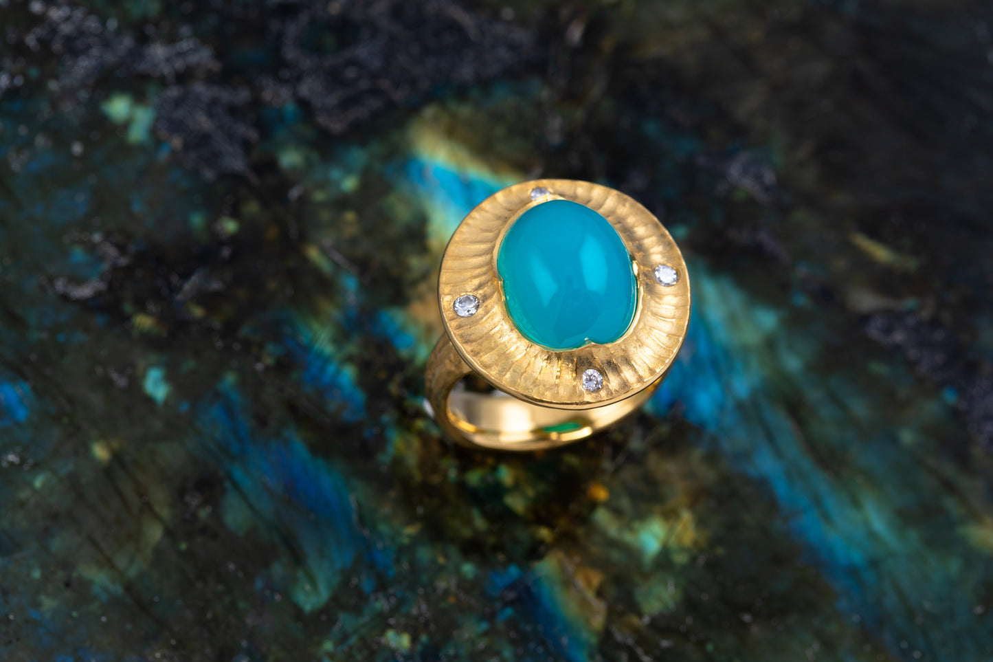 Gold ring with a blue chrysocolla stone on a textured green and black background
