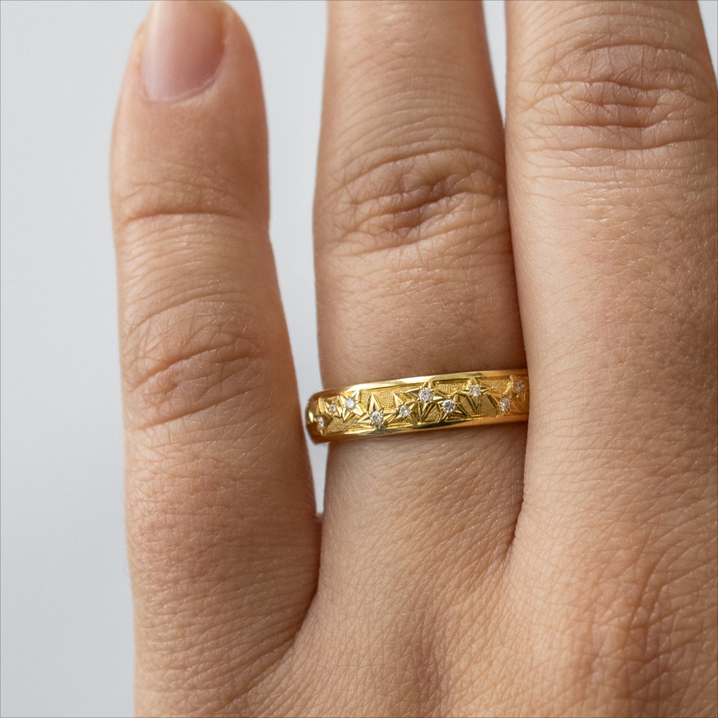 Yellow metal band featuring round gems and star pattern shown on a hand