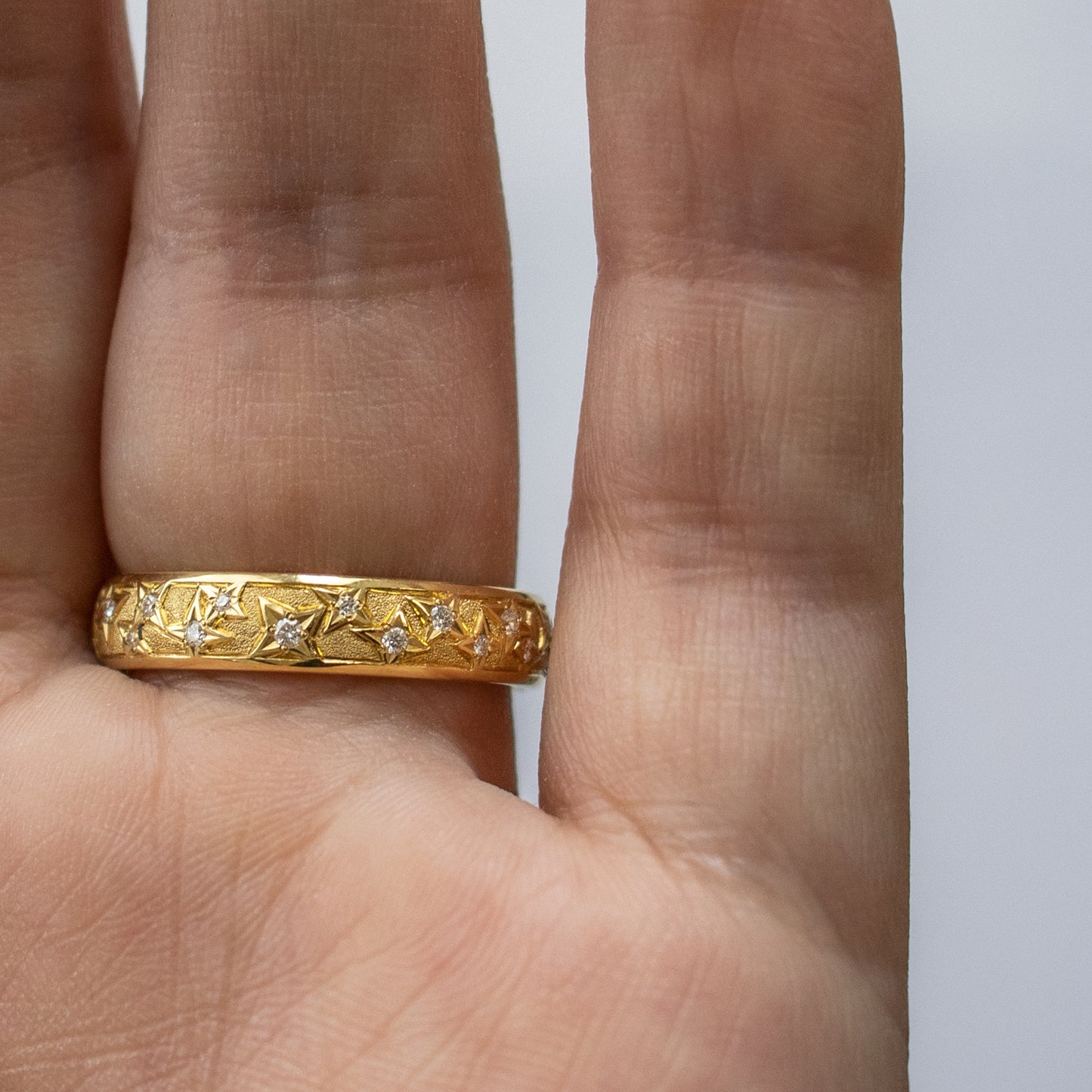 Yellow metal band featuring round gems and star pattern shown on a hand with palm facing camera
