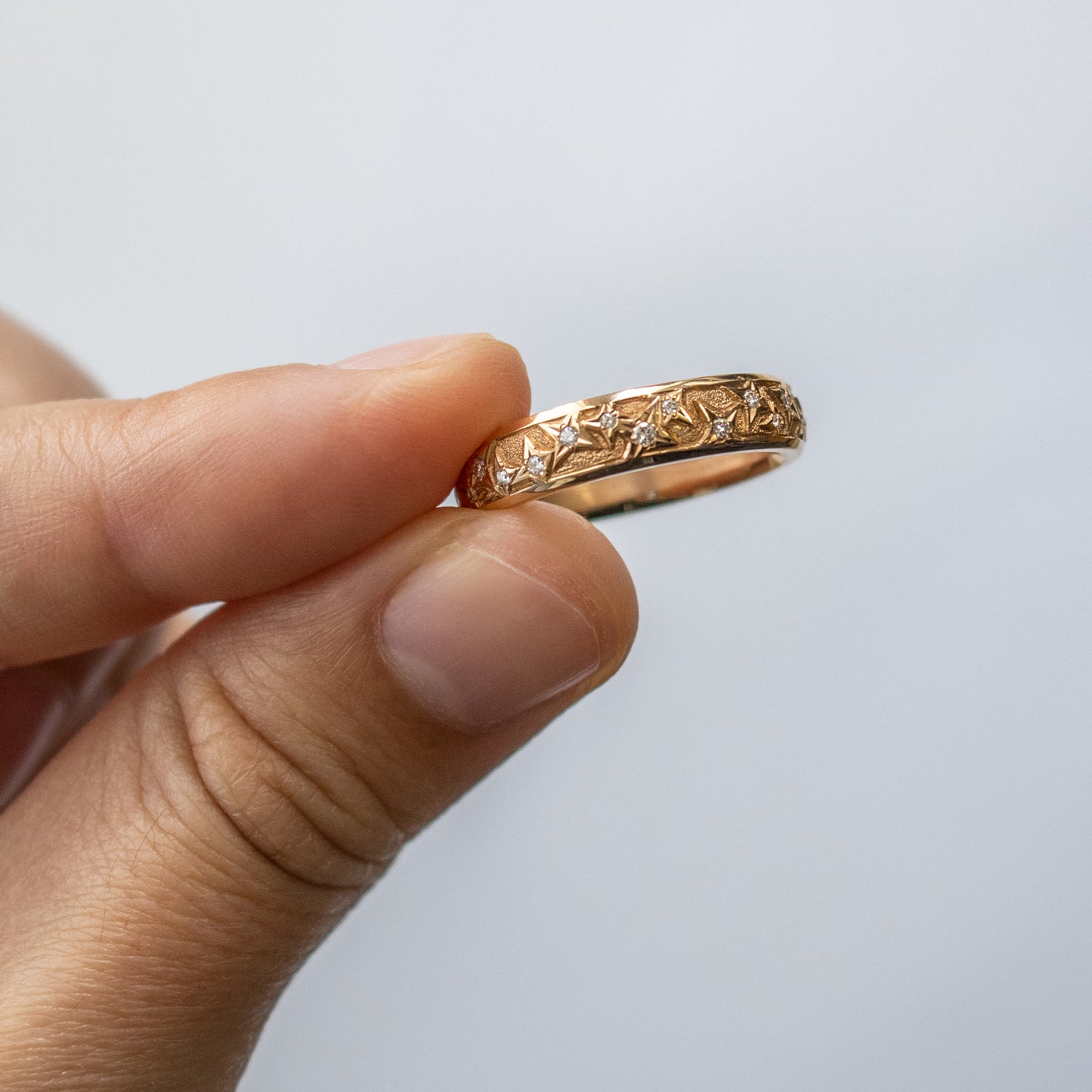 Held between fingers, an 18k rose gold band with round faceted diamonds.