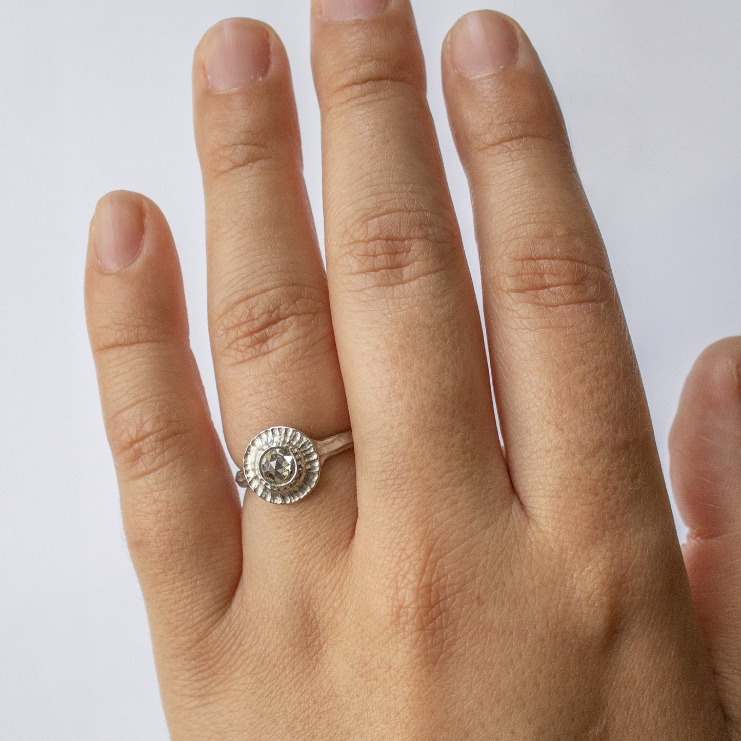 White metal ring with round gem worn on a hand