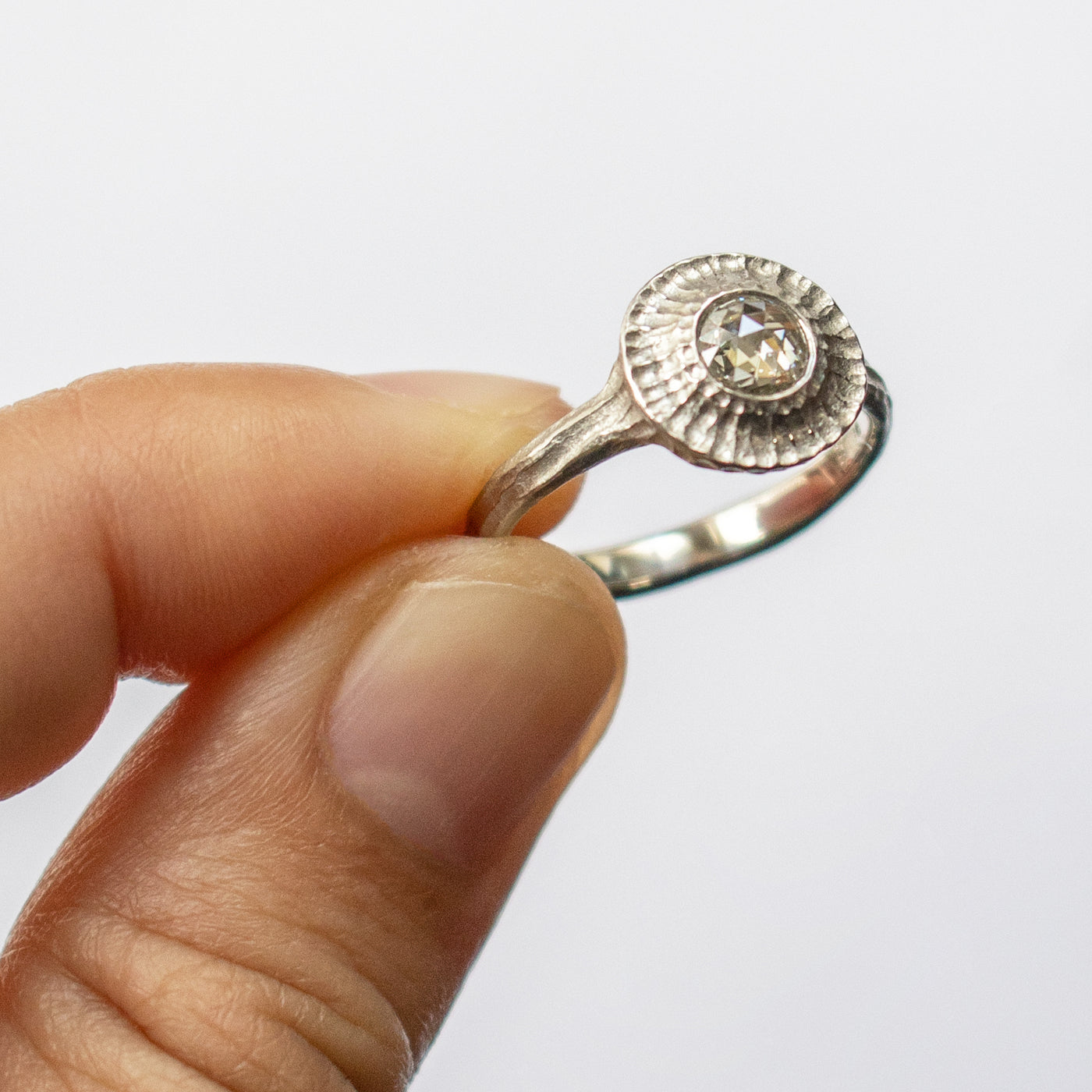 Fingers holding white metal ring with round gem