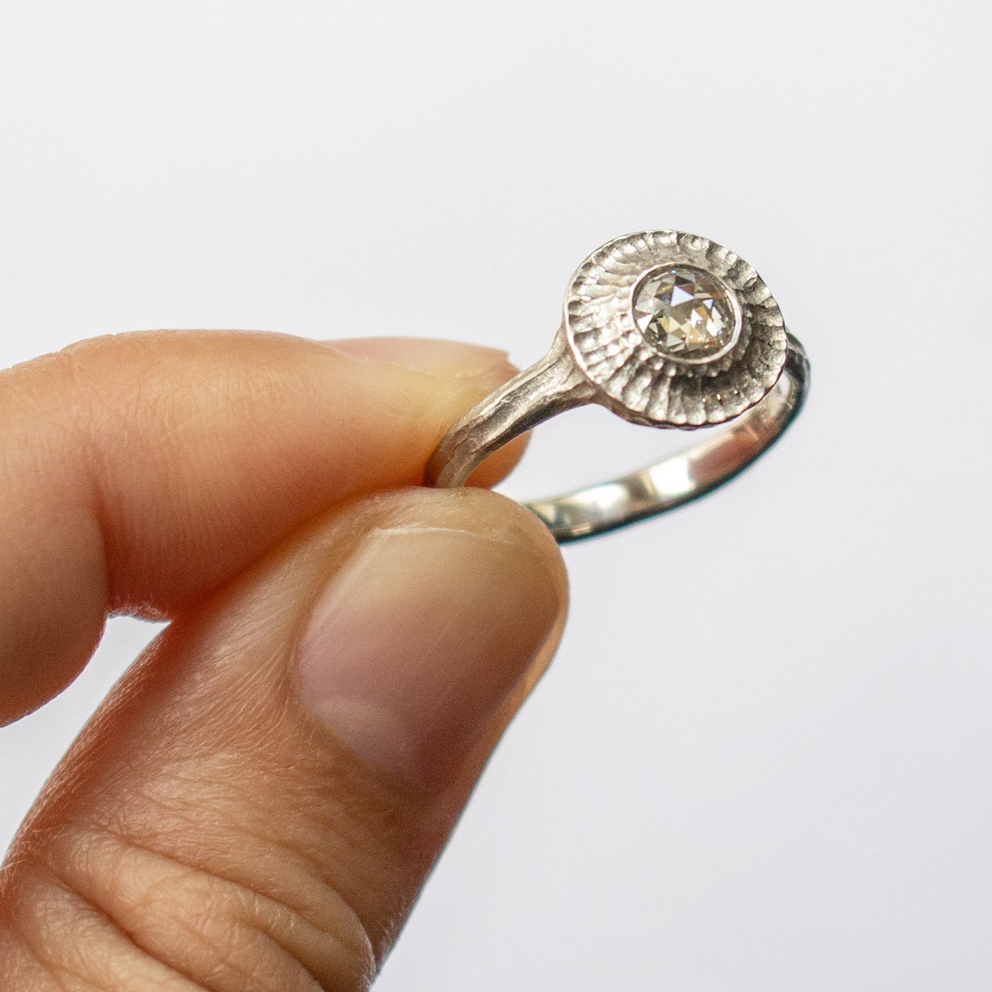 Fingers holding white metal ring with round gem