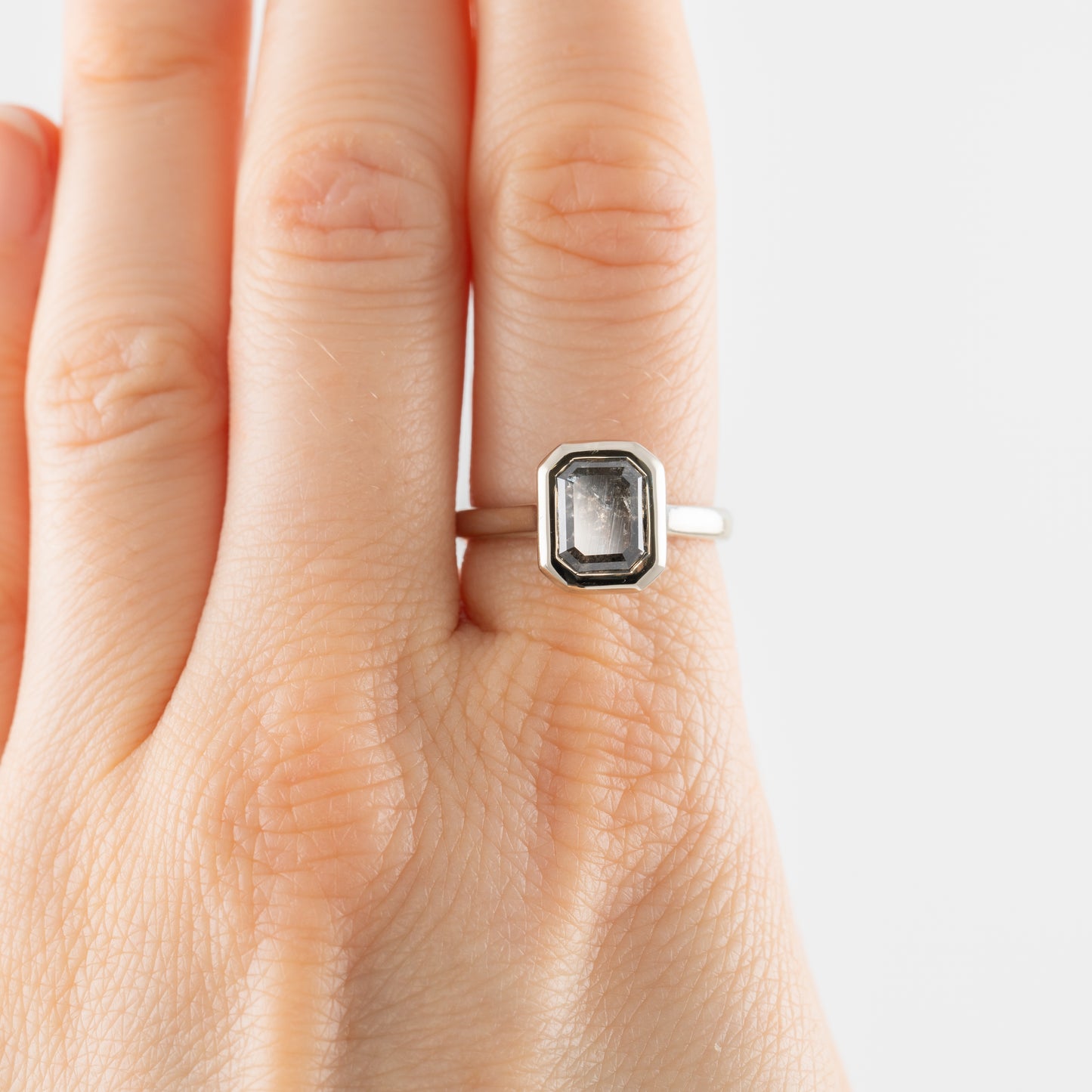 White gold ring with a gemstone on a hand against a white background