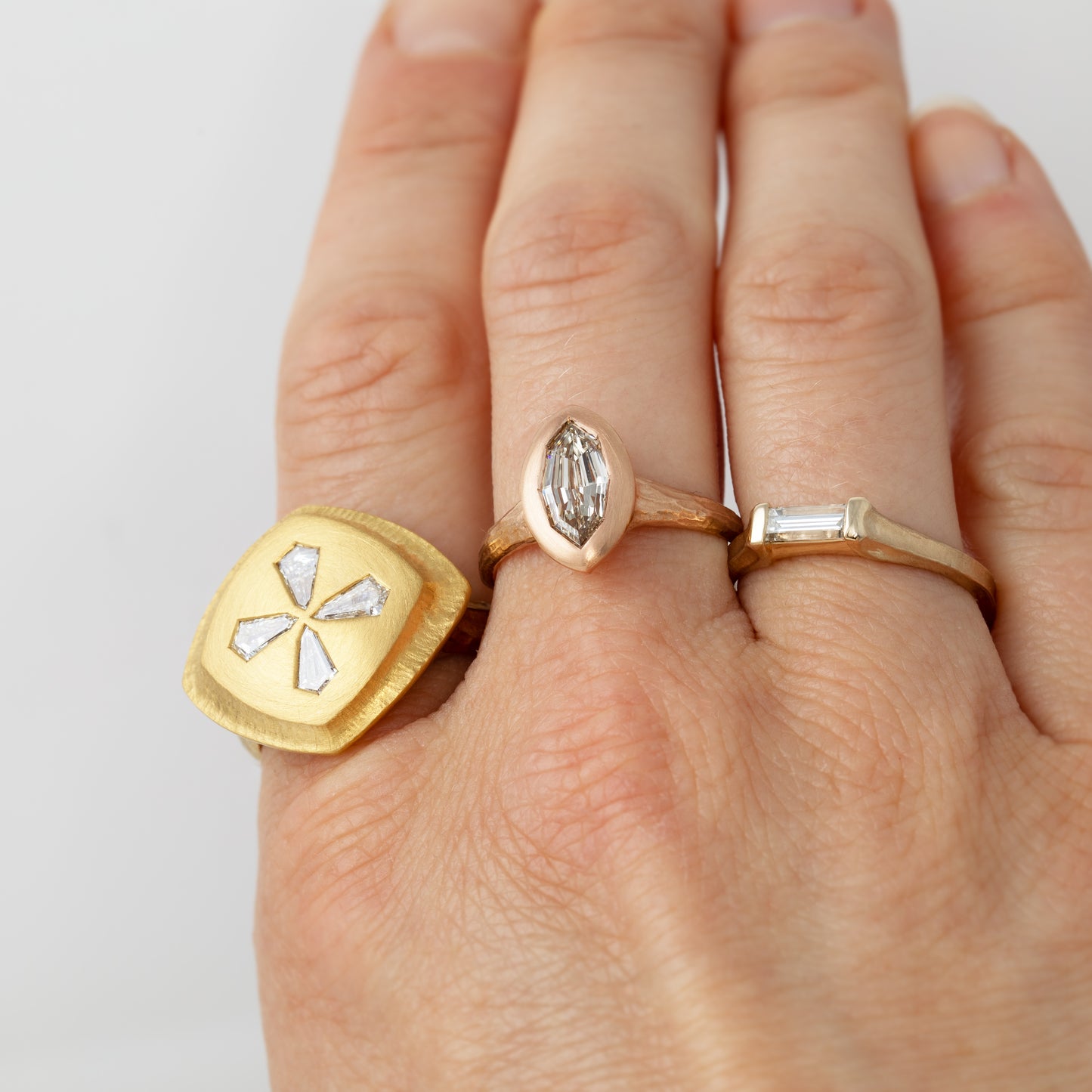 Hand wearing three gold rings with different designs on a light gray background