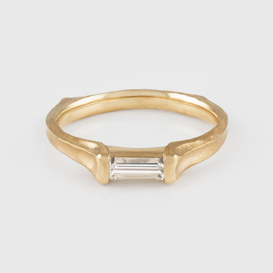 Gold ring with a baguette-cut diamond on a light gray background