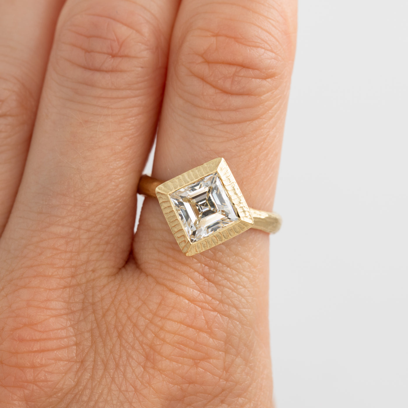 Gold ring with a diamond on a finger against a light background