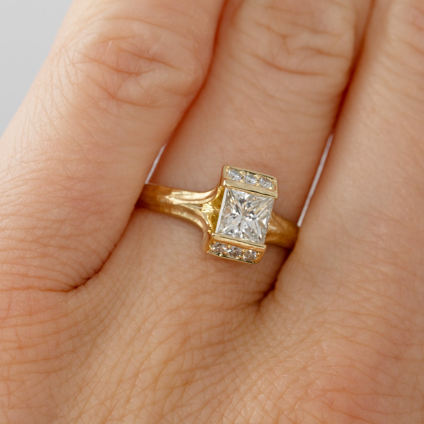 Gold ring with a diamond on a finger against a neutral background