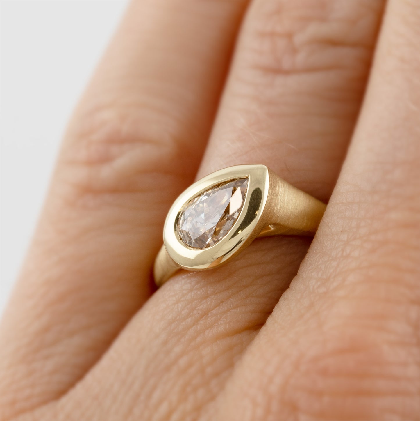 Yellow gold ring featuring bezel set pear brilliant champagne Diamond worn on a hand