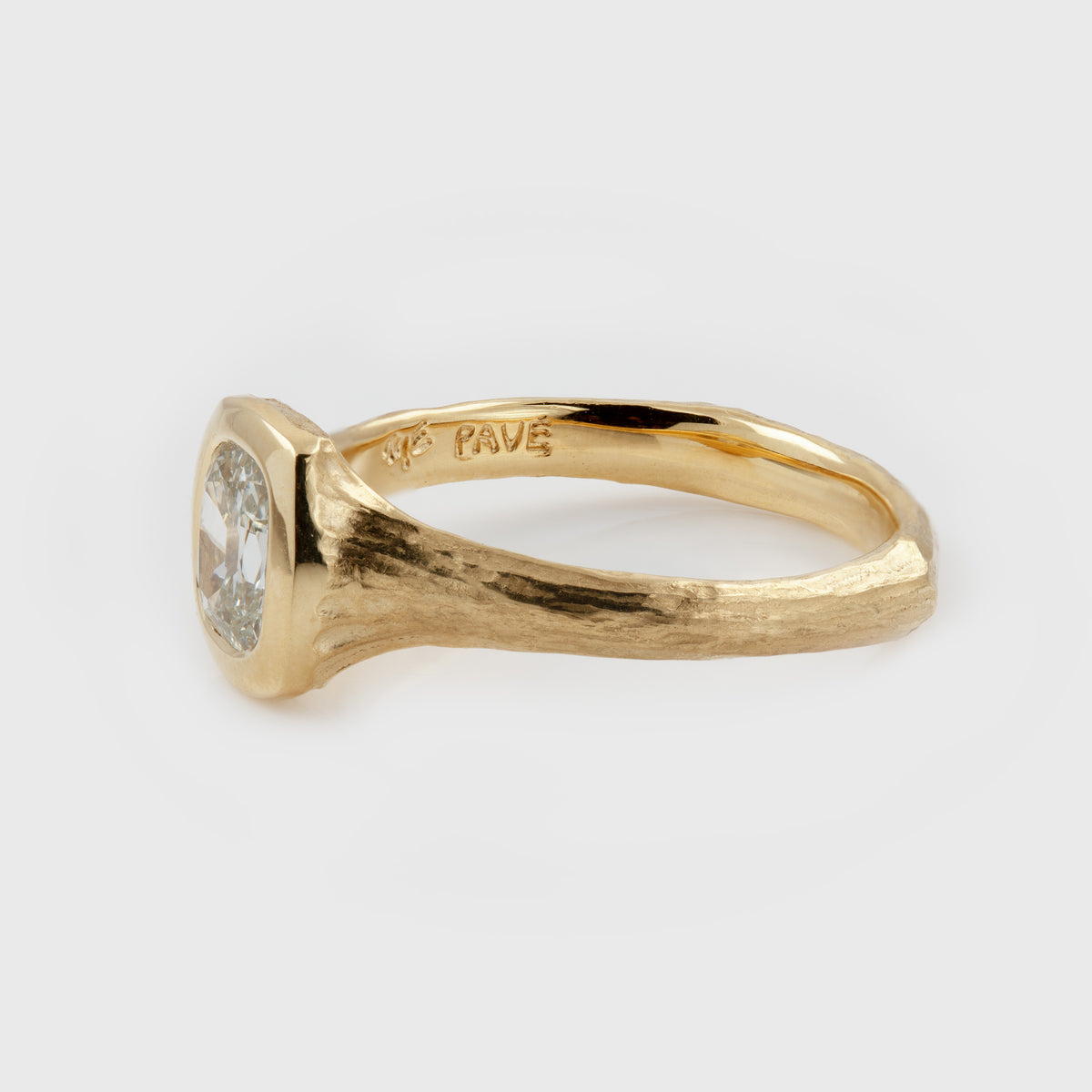 Side view of Yellow gold ring featuring a hybrid old-cut diamond center stone set in a high-polish bezel with a textured band, photographed on a white background. Band reads PAVE