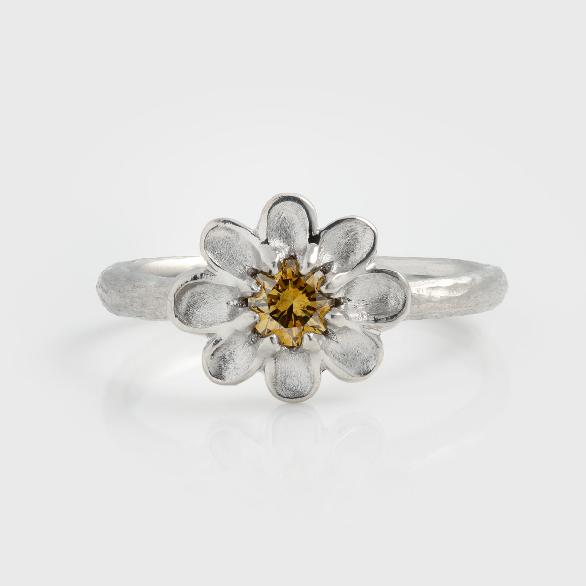 Platinum ring featuring a  yellow diamond center stone surrounded by brushed petal details and a textured band, photographed on a white background.