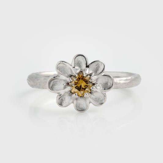 Platinum ring featuring a  yellow diamond center stone surrounded by brushed petal details and a textured band, photographed on a white background.