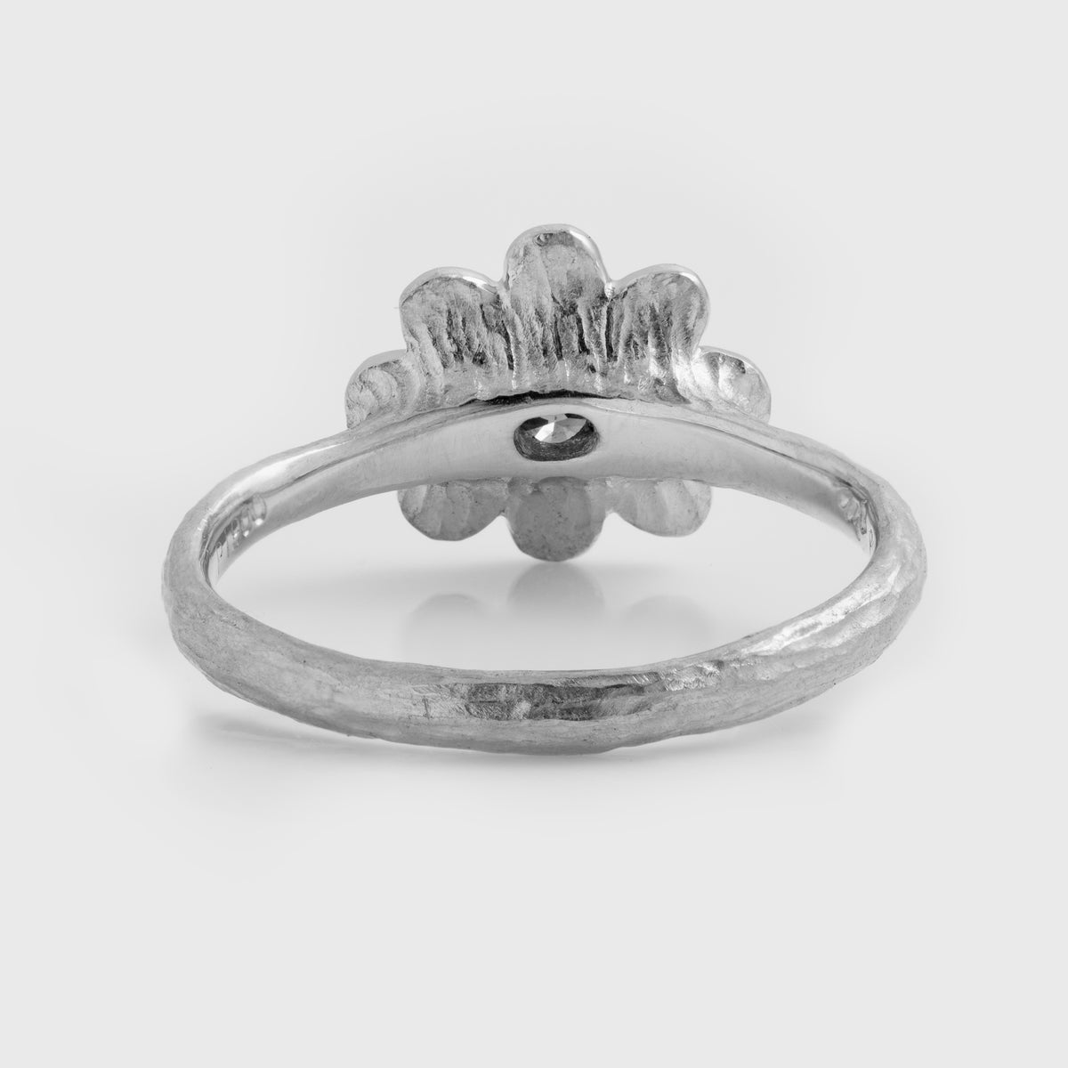 Rear view of platinum ring featuring a  yellow diamond center stone surrounded by brushed petal details and a textured band, photographed on a white 