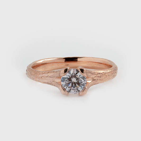 Rose gold ring featuring a light pink diamond center stone and a textured band, photographed on a white background.