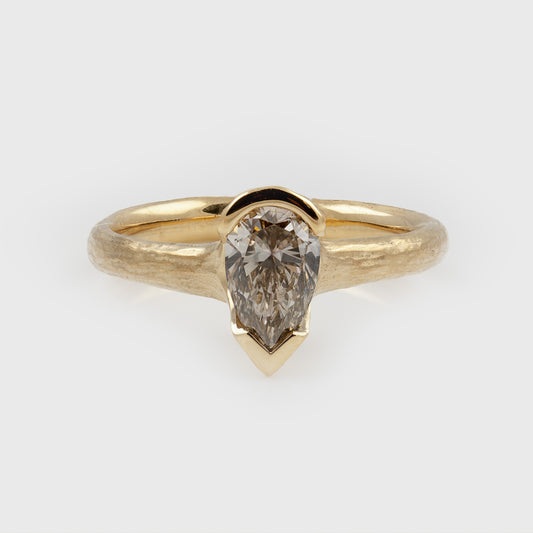 Yellow gold ring featuring a pear diamond center stone with a textured band, photographed on a white background.