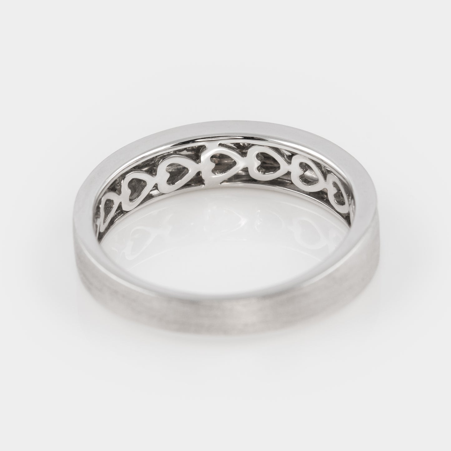 Silver ring with heart motif on the inner band, on a white background