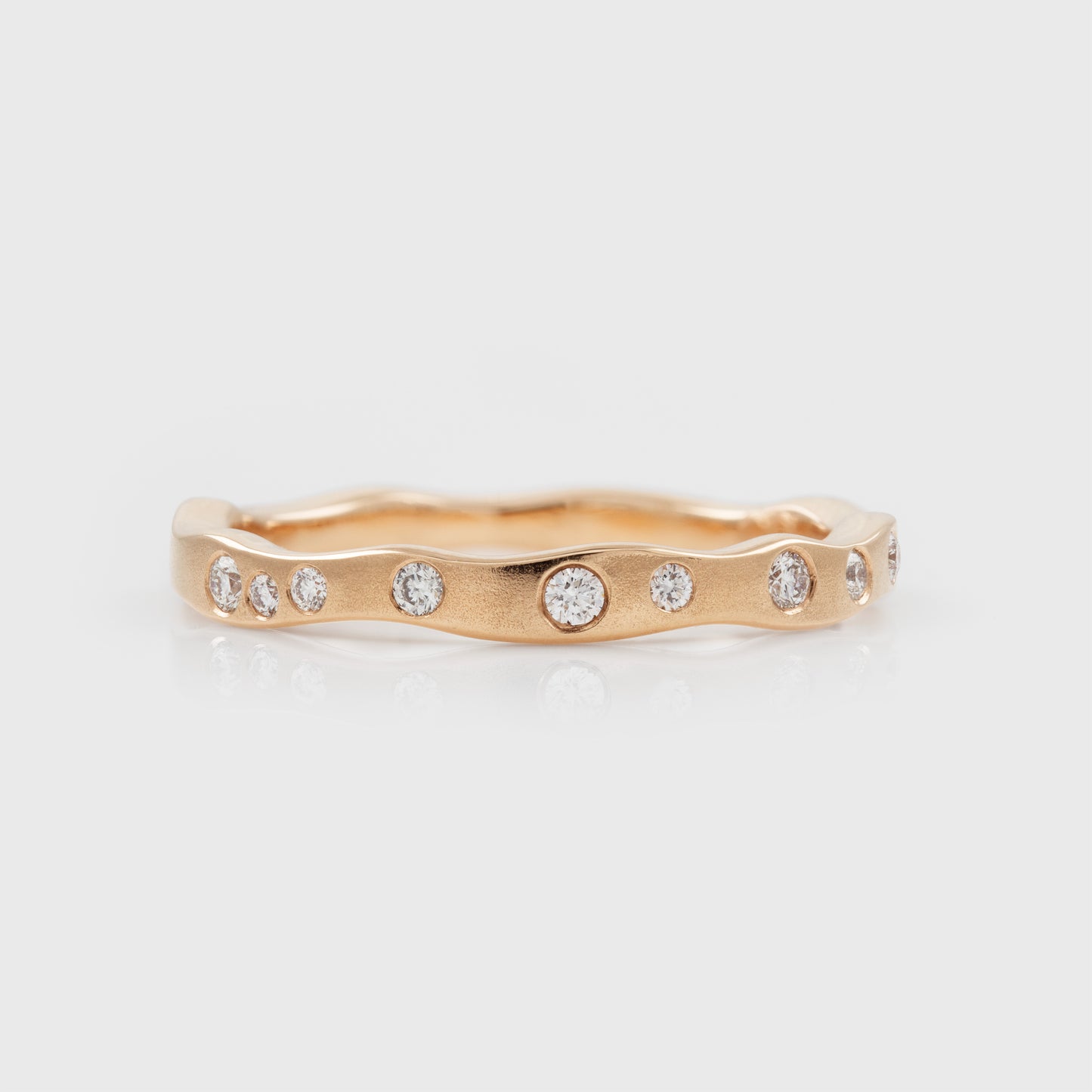 Rose gold ring with embedded diamonds on a light gray background