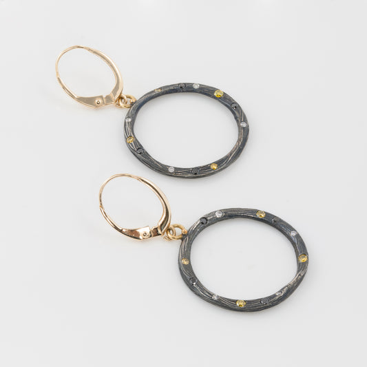 Pair of hoop earrings with gold and black design on a light gray background