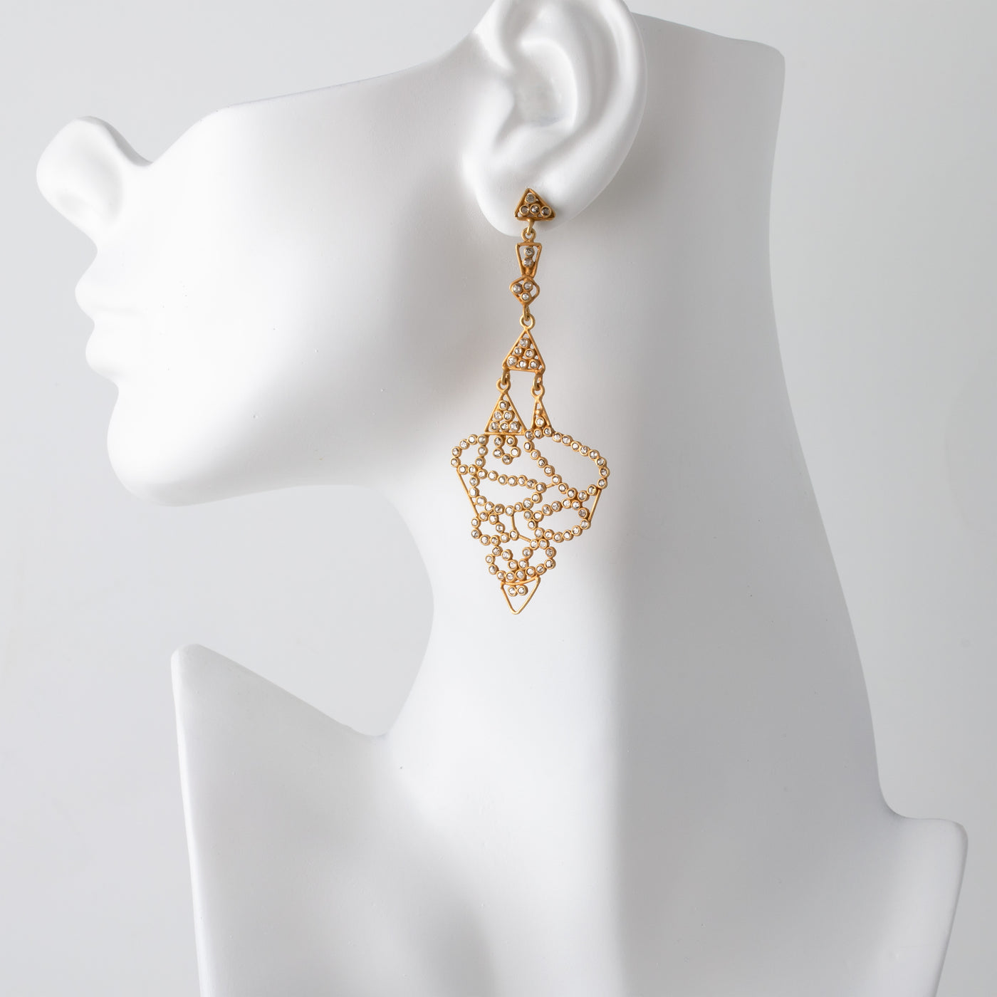 Gold earrings on a mannequin ear with a plain background