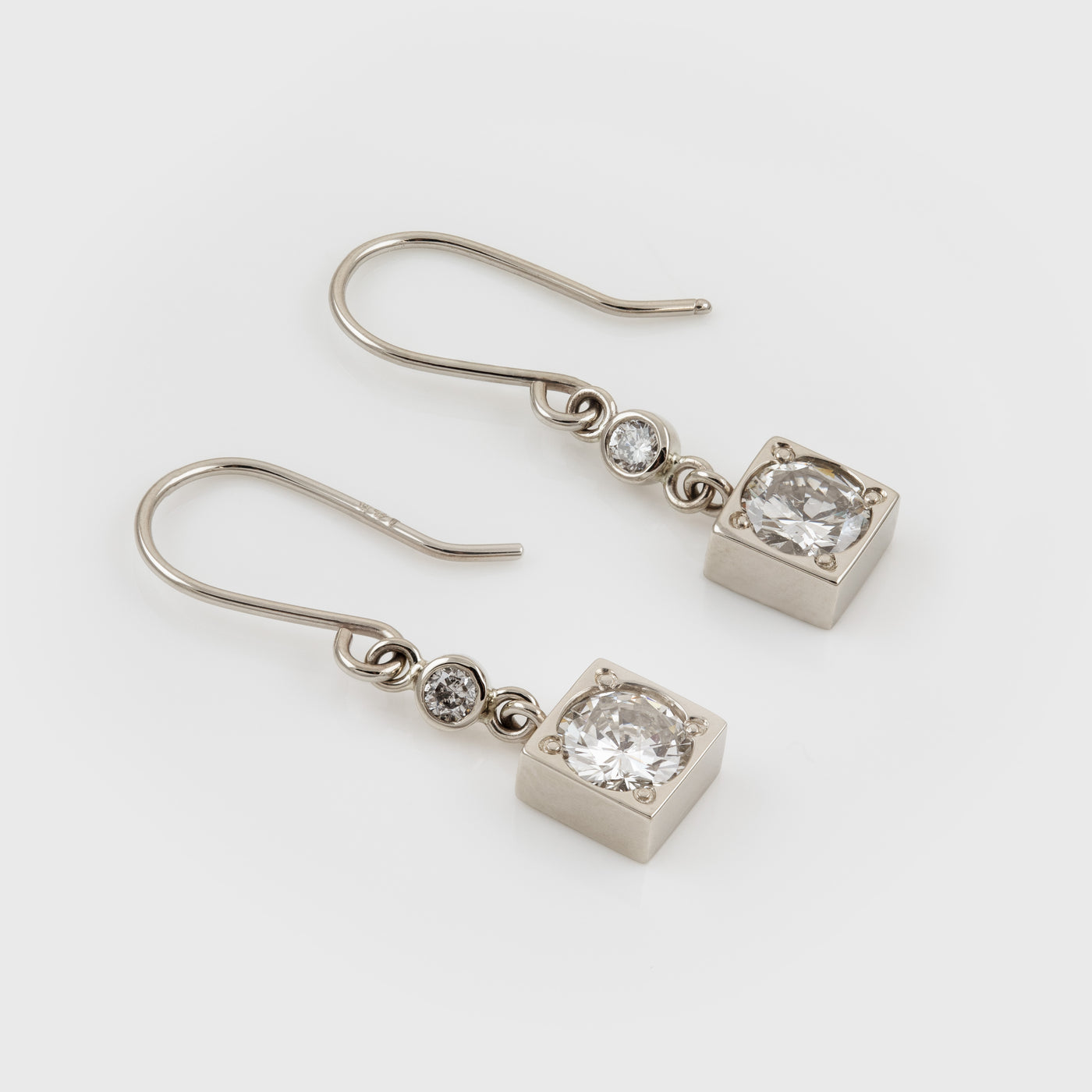 A pair of square silver-toned drop earrings featuring diamonds and small round accent diamonds, displayed on a clean light gray background.