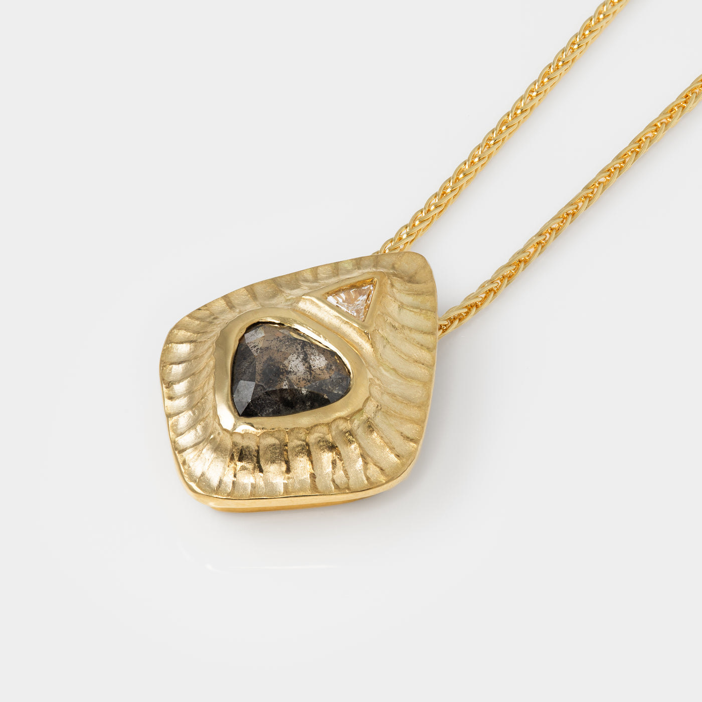 Gold necklace with a textured pendant and salt and pepper diamond on a white background