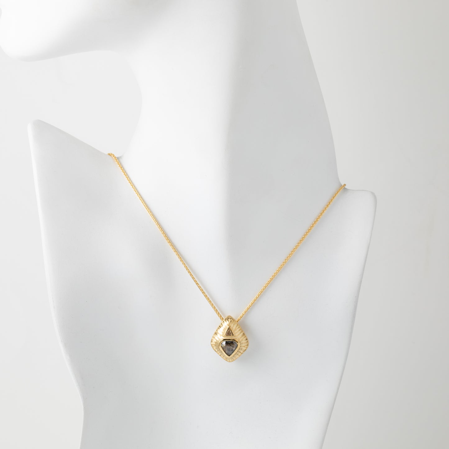 Gold necklace with a triangle-shaped pendant on a mannequin bust.