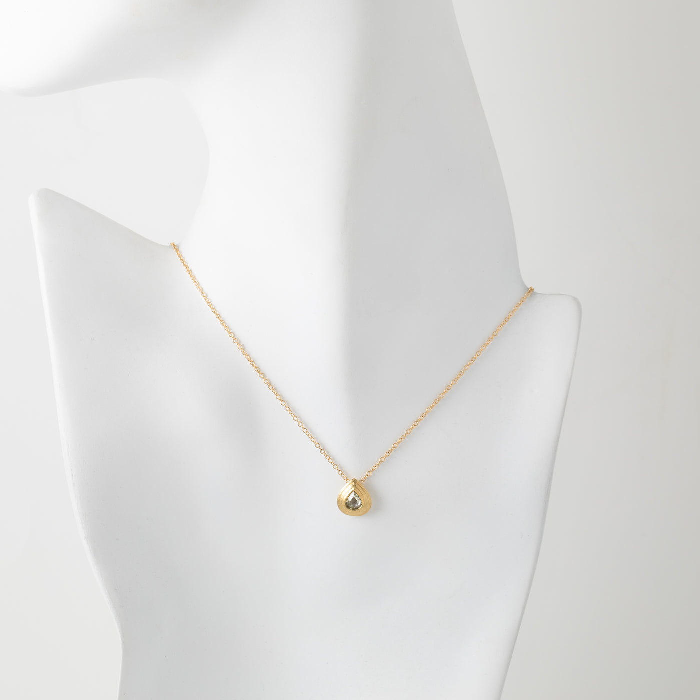 Gold necklace with a small pendant on a mannequin bust against a white background