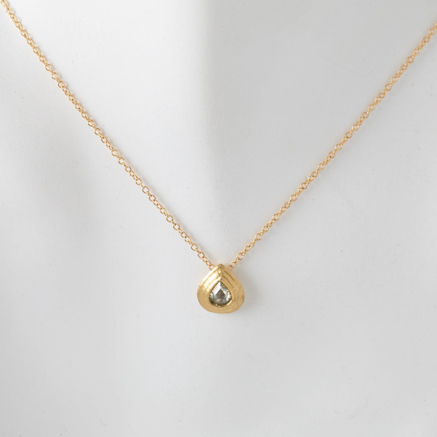Gold necklace with a teardrop-shaped pendant, close-up shot on white mannequin