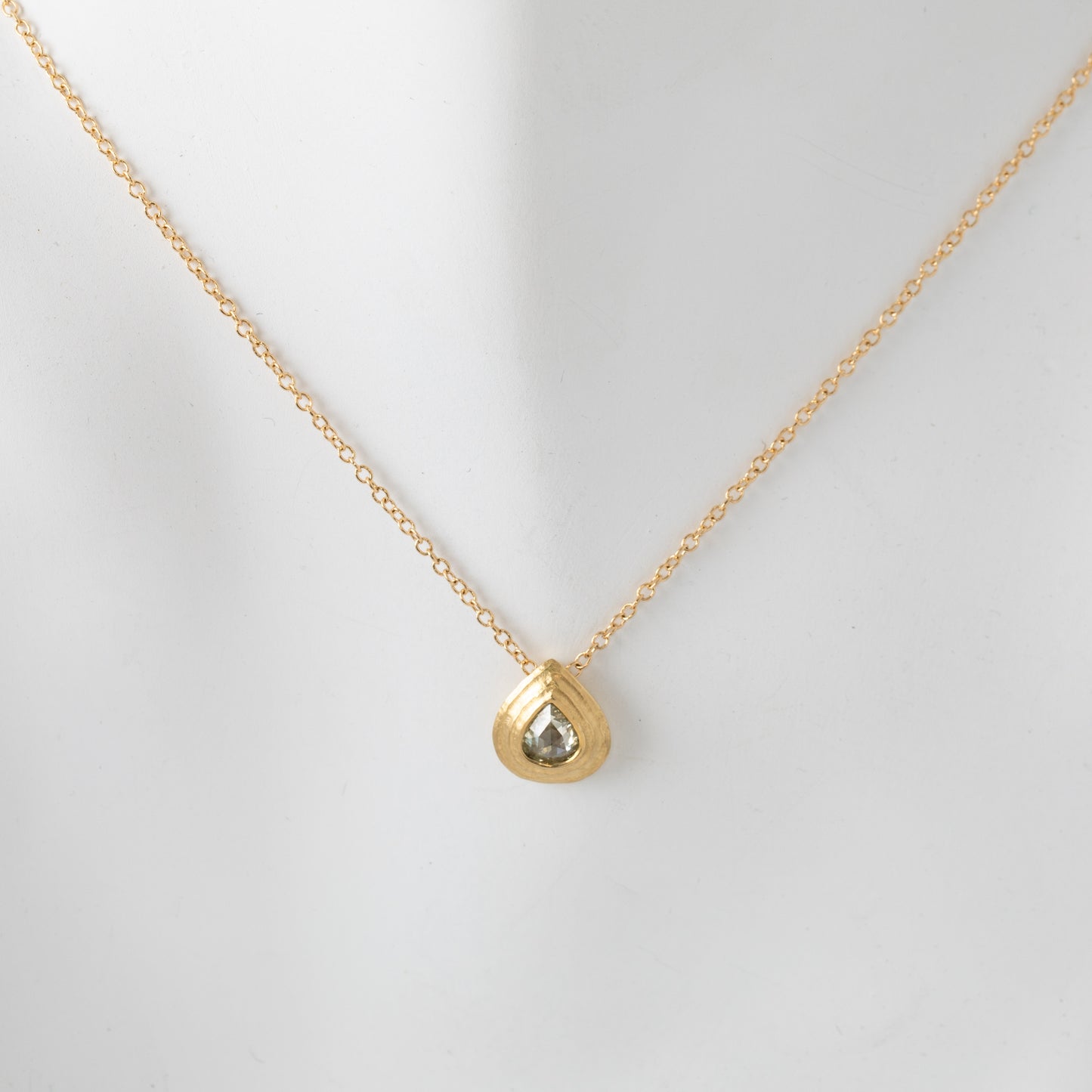 Gold necklace with a teardrop-shaped pendant, close-up shot on white mannequin