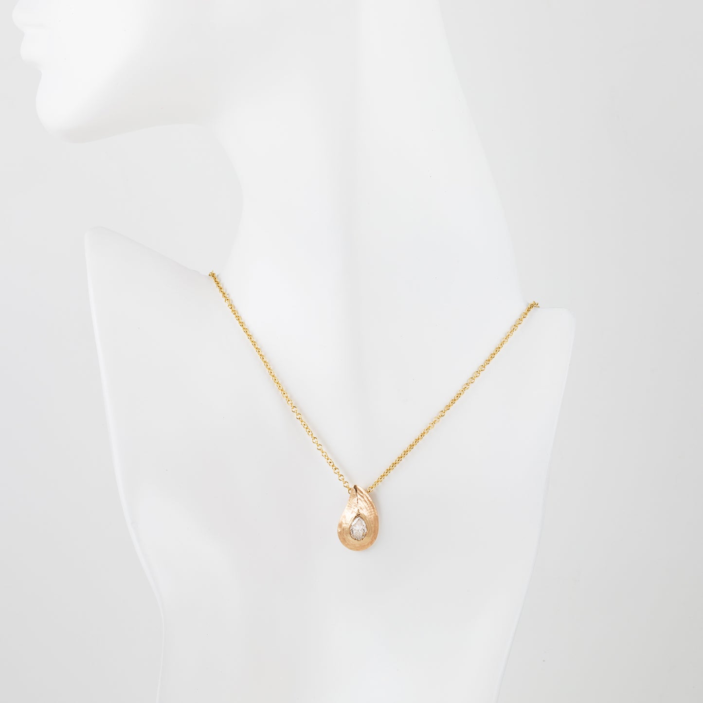 Pear shaped gold pendant with redwood bark texture on white mannequin