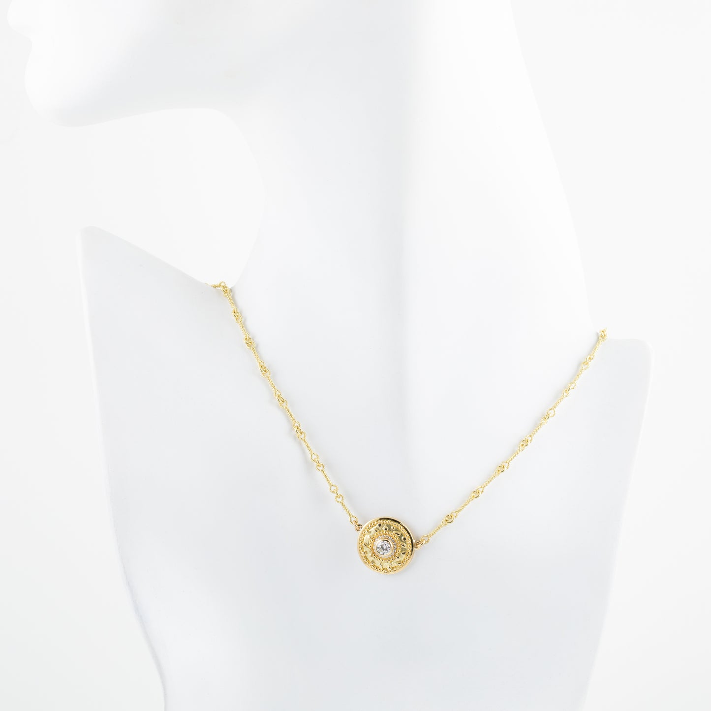 Gold necklace with a circular pendant on a white mannequin