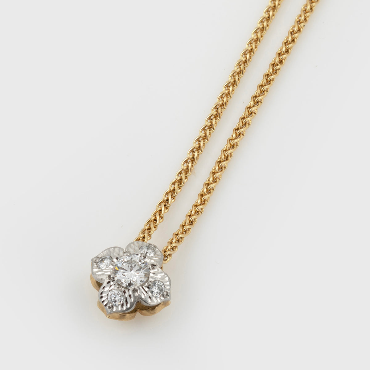 Two-tone flower pendant featuring diamonds, suspended from a yellow gold chain, photographed on a white background.