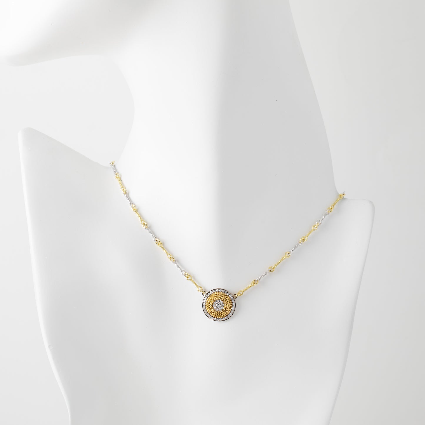 Gold necklace with a circular pendant on a mannequin bust against a white background