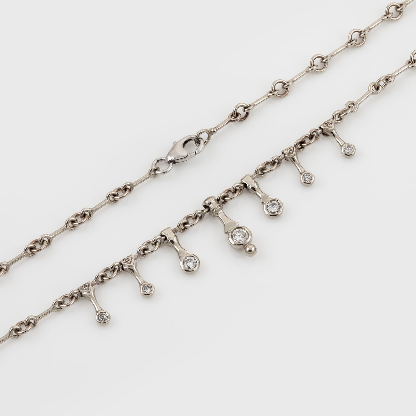 A silver-toned chain necklace with a dangling charm line featuring small diamonds, photographed on a clean white background.