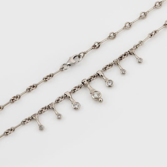 A silver-toned chain necklace with a dangling charm line featuring small diamonds, photographed on a clean white background.