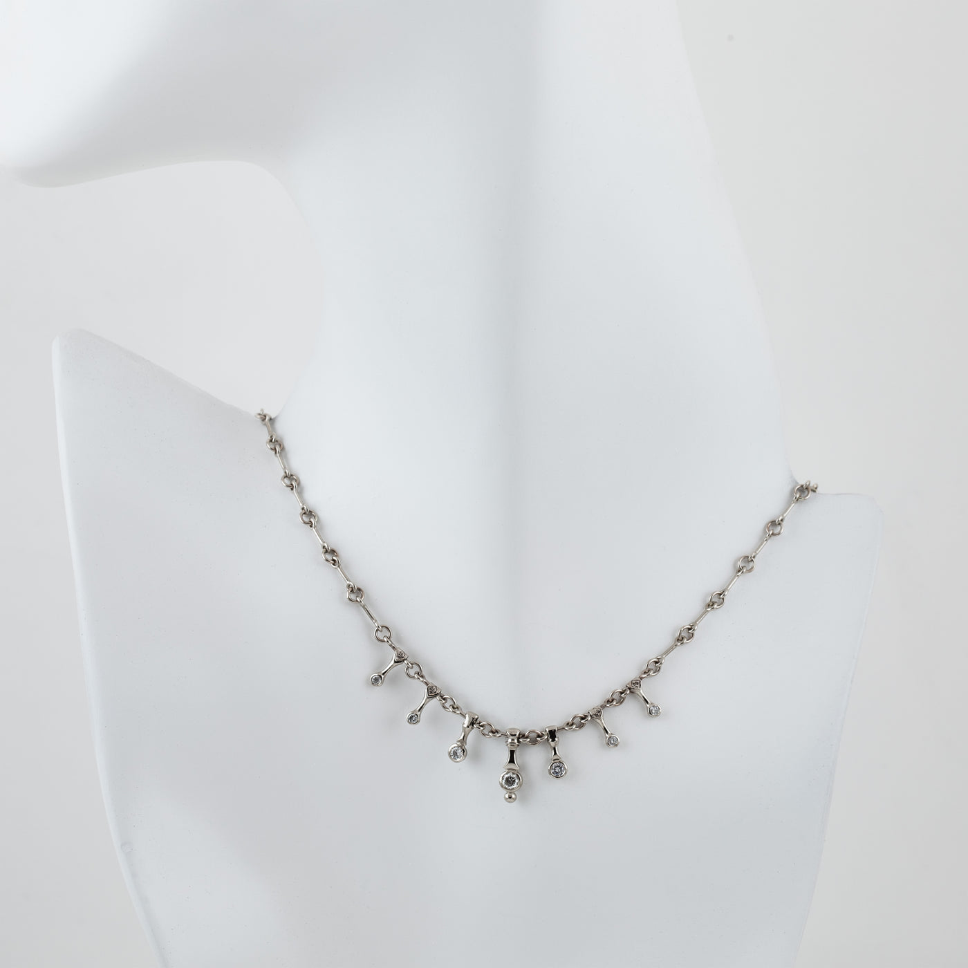 A silver-toned necklace displayed on a white mannequin bust against a white background.