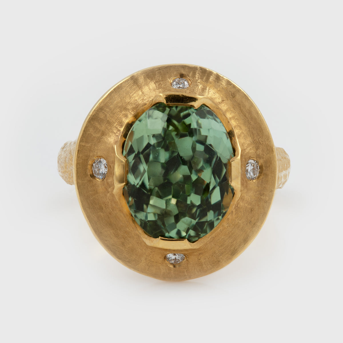 A gold ring featuring a large, faceted green gemstone in the center, surrounded by a textured gold band with four small diamonds, photographed on a white background.