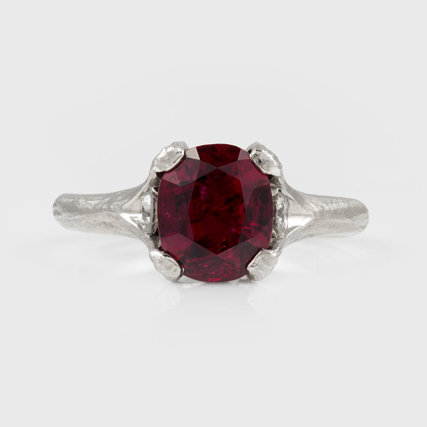 A platinum ring featuring a large deep red ruby gemstone with a textured band, shown on a light gray background.