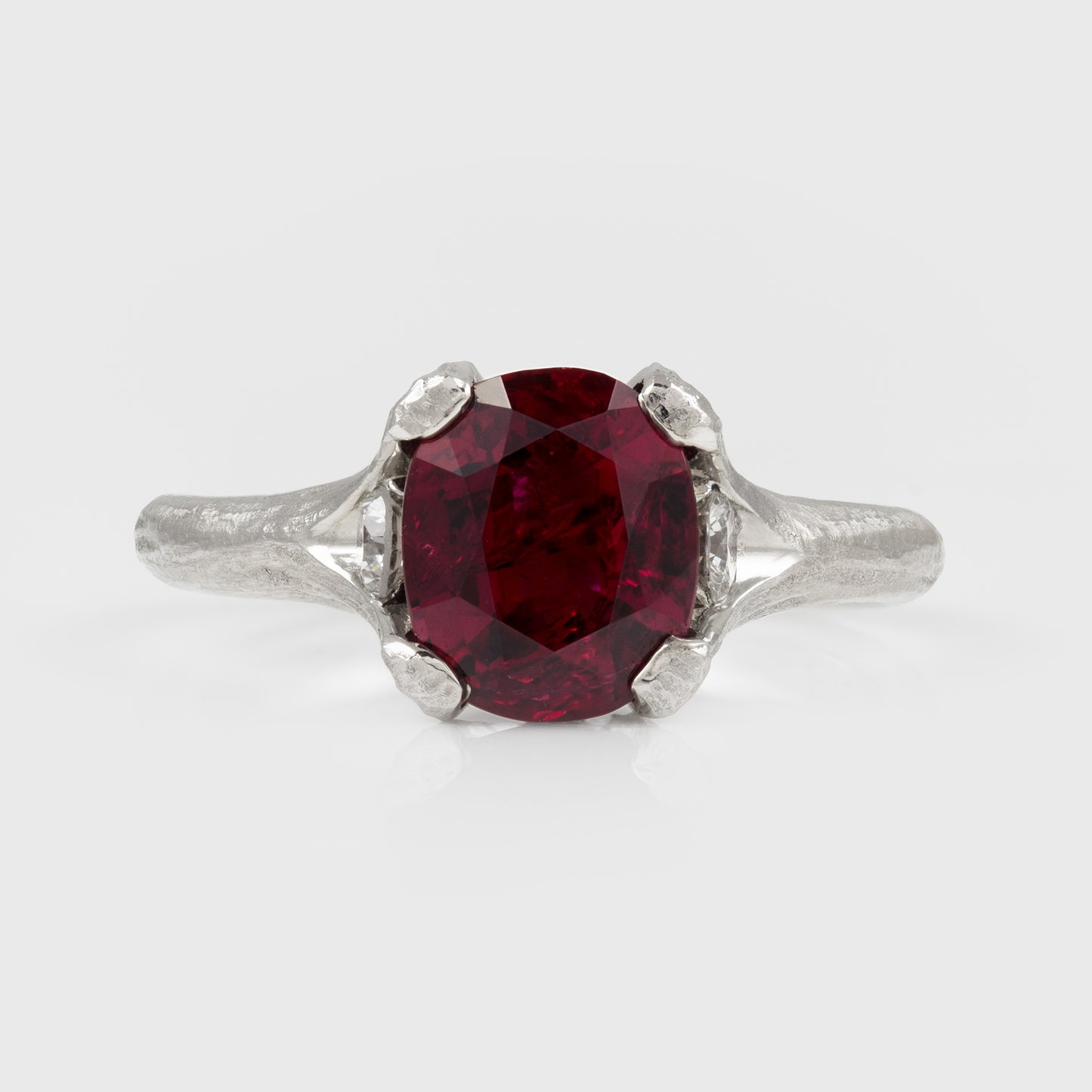 A platinum ring featuring a large deep red ruby gemstone with a textured band, shown on a light gray background.