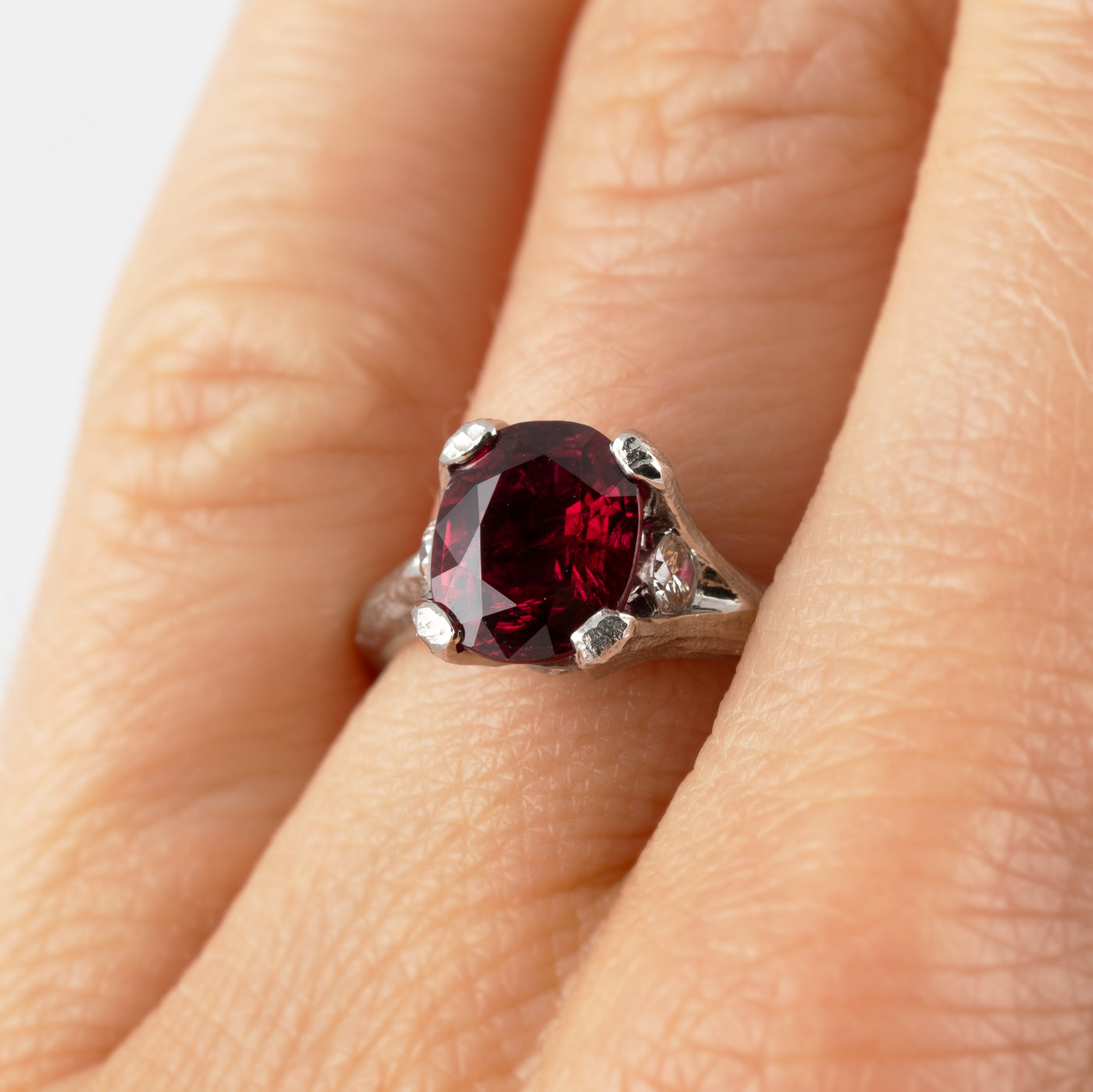 A platinum ring featuring a large deep red ruby gemstone with a textured band, shown on a hand