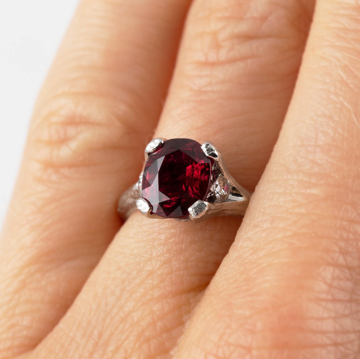 A platinum ring featuring a large deep red ruby gemstone with a textured band, shown on a hand