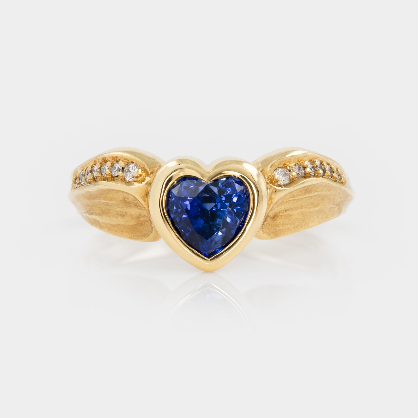 Gold ring with a heart-shaped blue gemstone on a white background