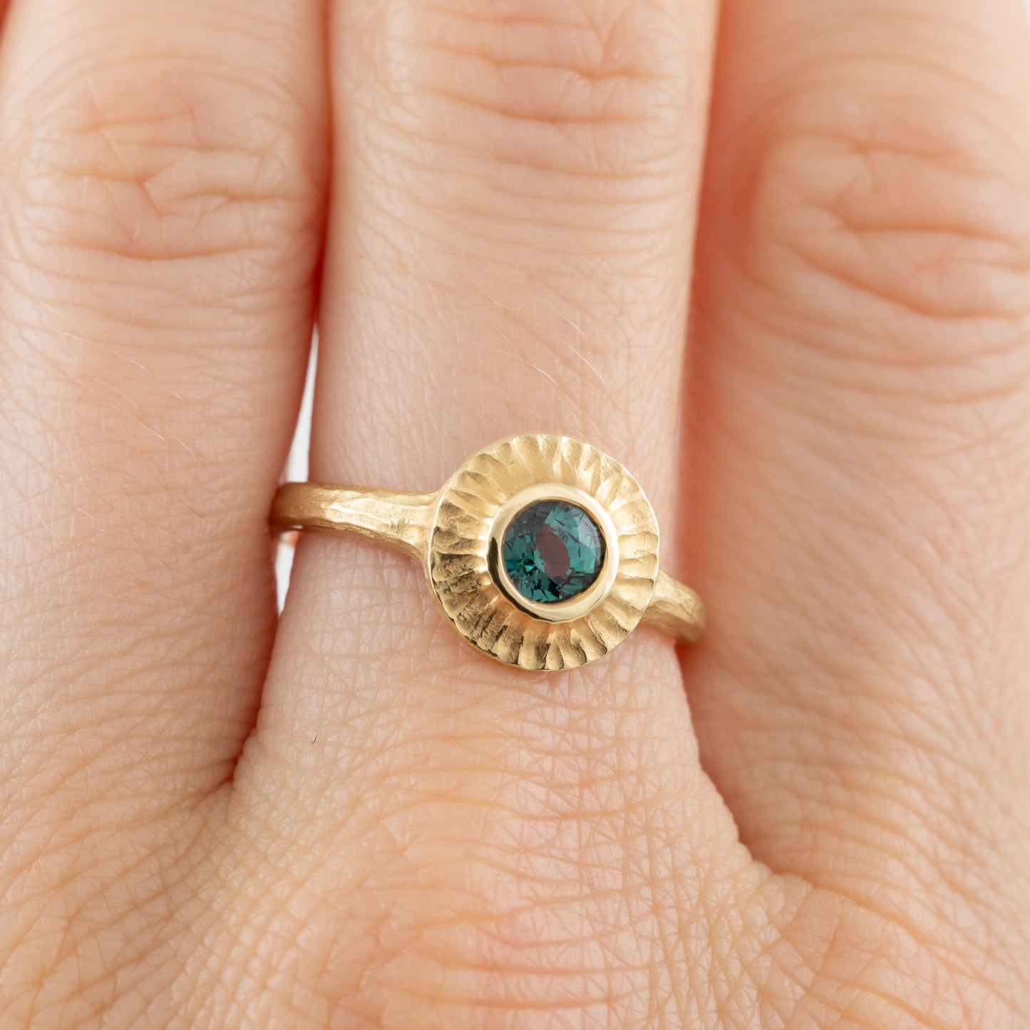 Gold ring with a green gemstone on a finger