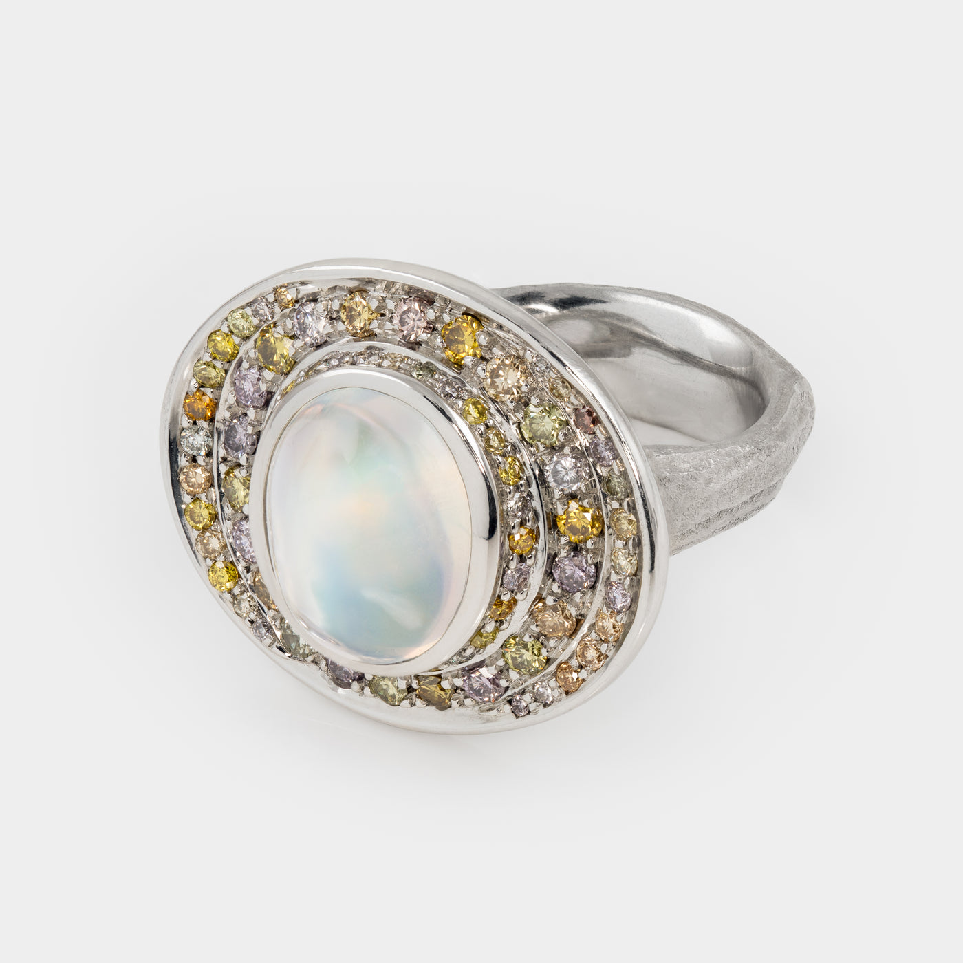 Side view of platinum ring with a central moonstone surrounded by multicolored diamonds on a white background