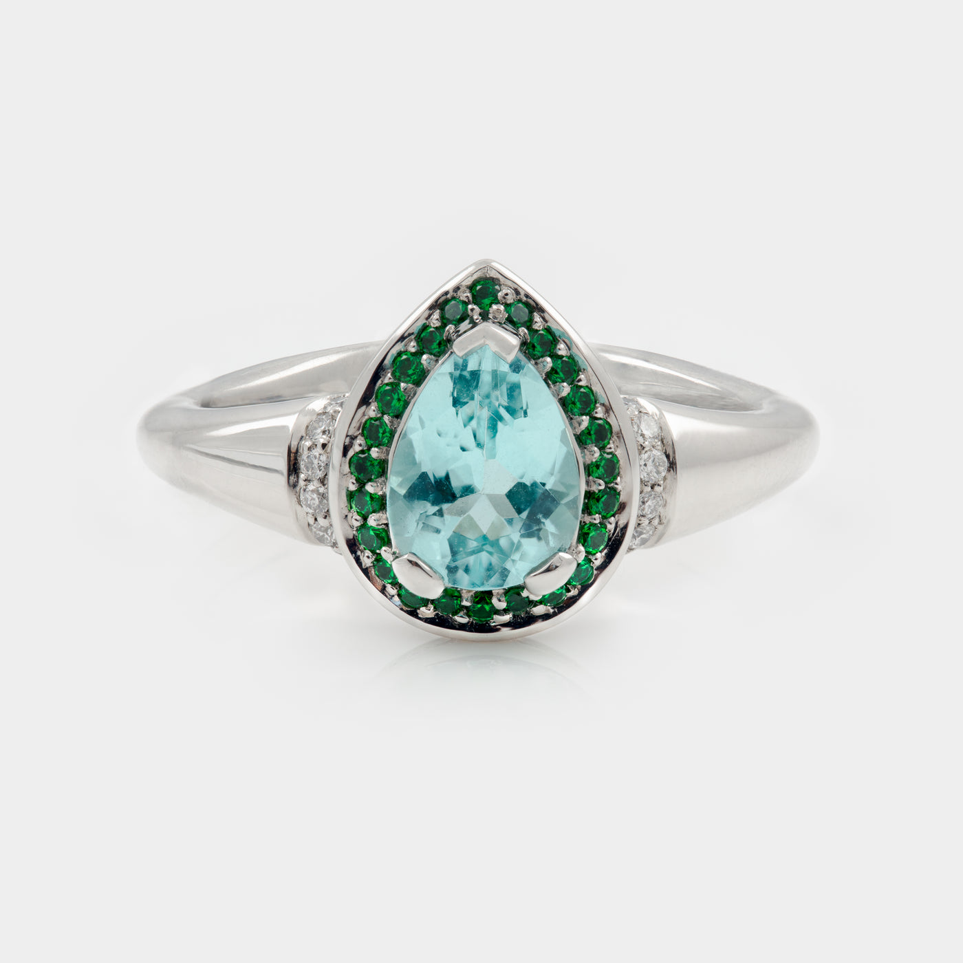Platinum ring with a pear-shaped blue gemstone and green accents on a white background