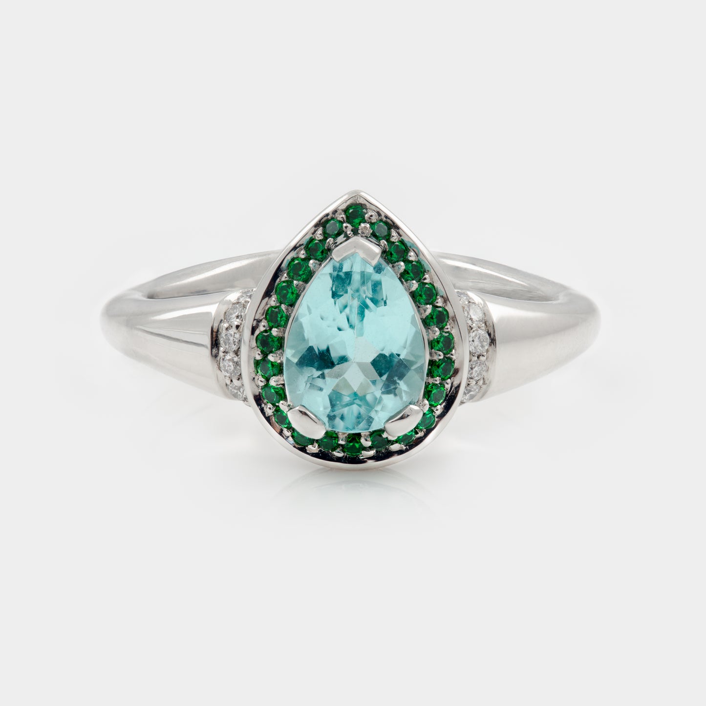 Platinum ring with a pear-shaped blue gemstone and green accents on a white background