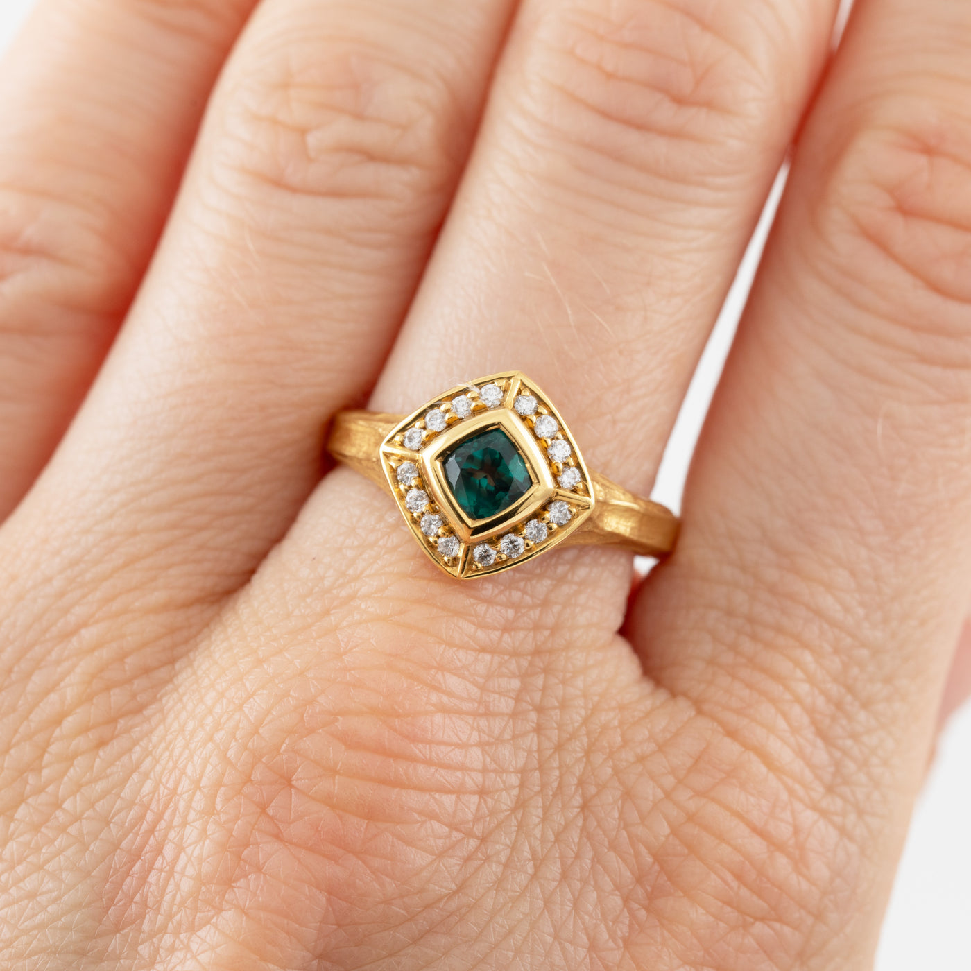 Gold ring with a green Alexandrite gemstone and diamond accents on a hand